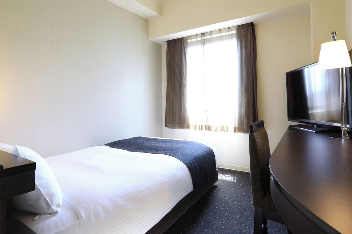 A hotel room with a bed, a desk with a lamp, and a television.