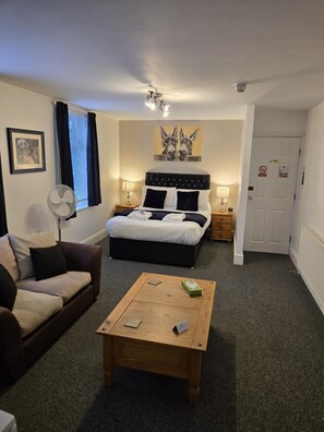 A bedroom with a bed, bedside tables, a fan, a couch, and a coffee table. - Q Accommodation (Blackpool)