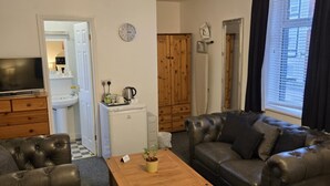 A living room with a sofa, a coffee table, a television, and a kitchen area in the background. - Q Accommodation (Blackpool)
