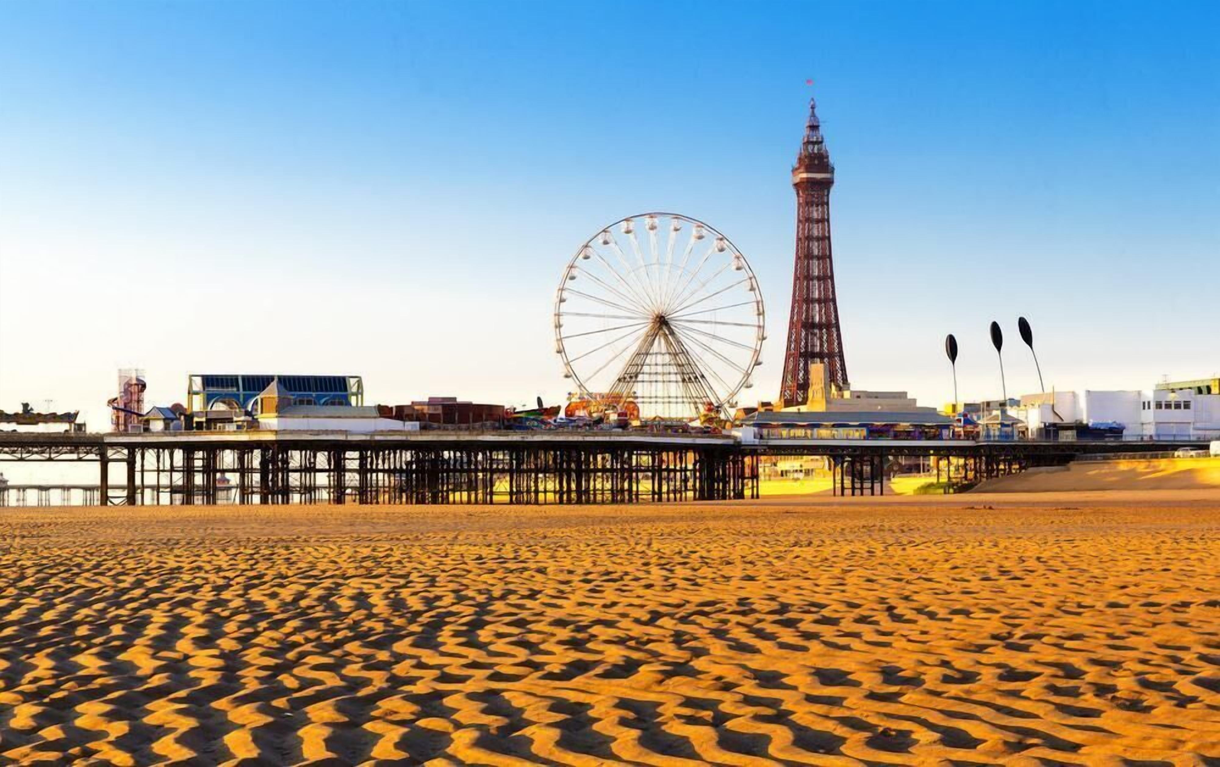 A beach with a Ferris wheel, a tall tower, and a pier.