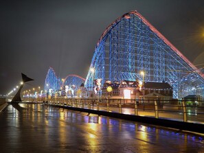 A brightly lit roller coaster at night with a metal framework and colorful lights. - Q Accommodation (Blackpool)