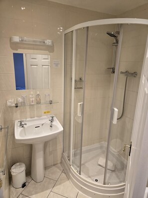 A modern bathroom with a curved shower enclosure, a pedestal sink, and a glass shower door. - Q Accommodation (Blackpool)
