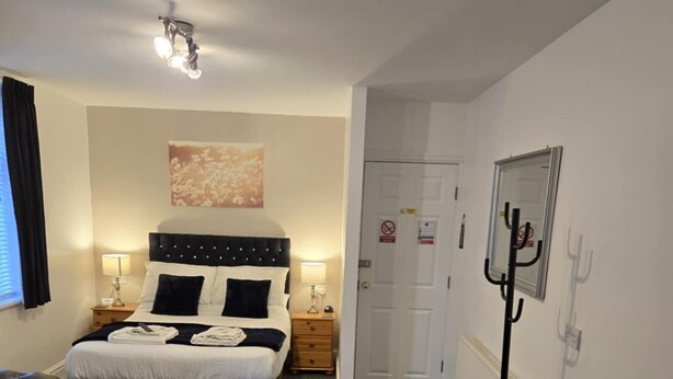 A hotel room with a bed, a wooden coffee table, a leather sofa, and a wall-mounted coat rack. - Q Accommodation (Blackpool)