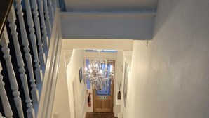 A staircase with white balusters leading to a wooden door with a chandelier above. - Q Accommodation (Blackpool)