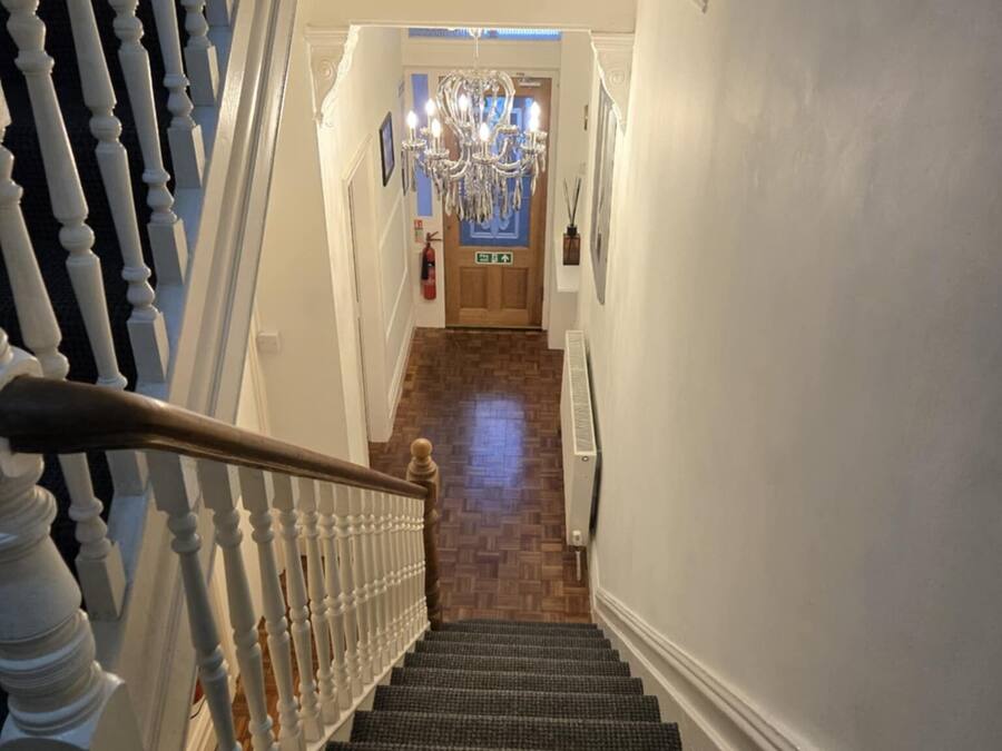 Una escalera con barandillas blancas que lleva a una puerta de madera con una araña colgante.