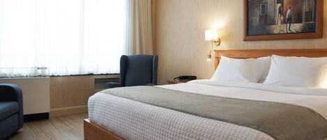 Habitación de hotel con una cama grande, una silla, un cuadro en la pared y un ventanal con cortinas.