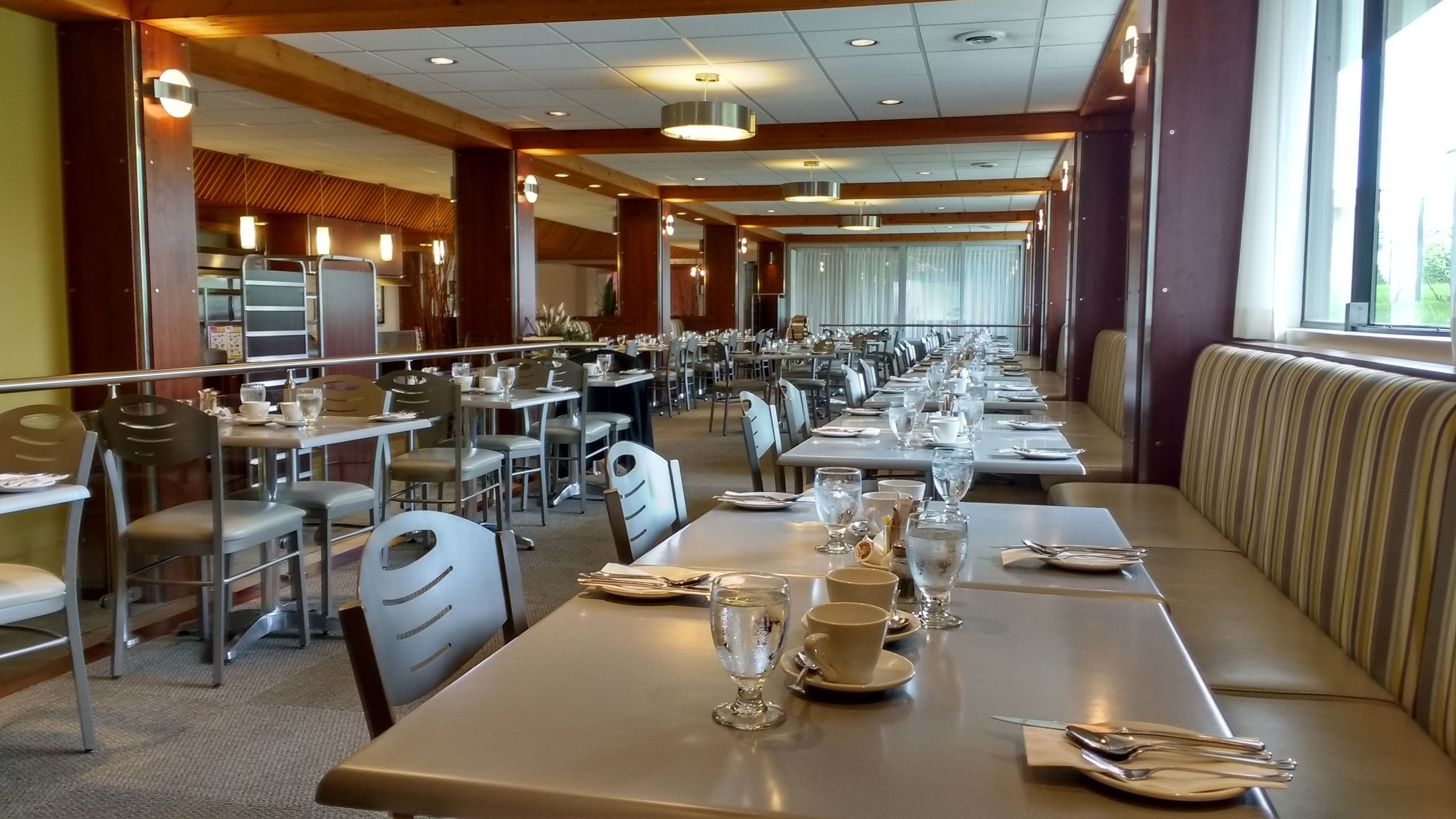 Un comedor amplio con varias mesas y sillas, ventanas grandes y un techo alto con iluminación empotrada.