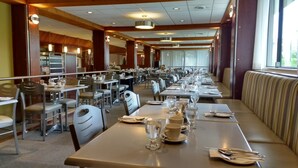 A spacious dining area with multiple tables and chairs, large windows, and a high ceiling with recessed lighting.