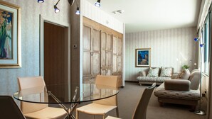 A modern living room with a glass dining table, beige sofas, and a kitchen area with wooden cabinets.