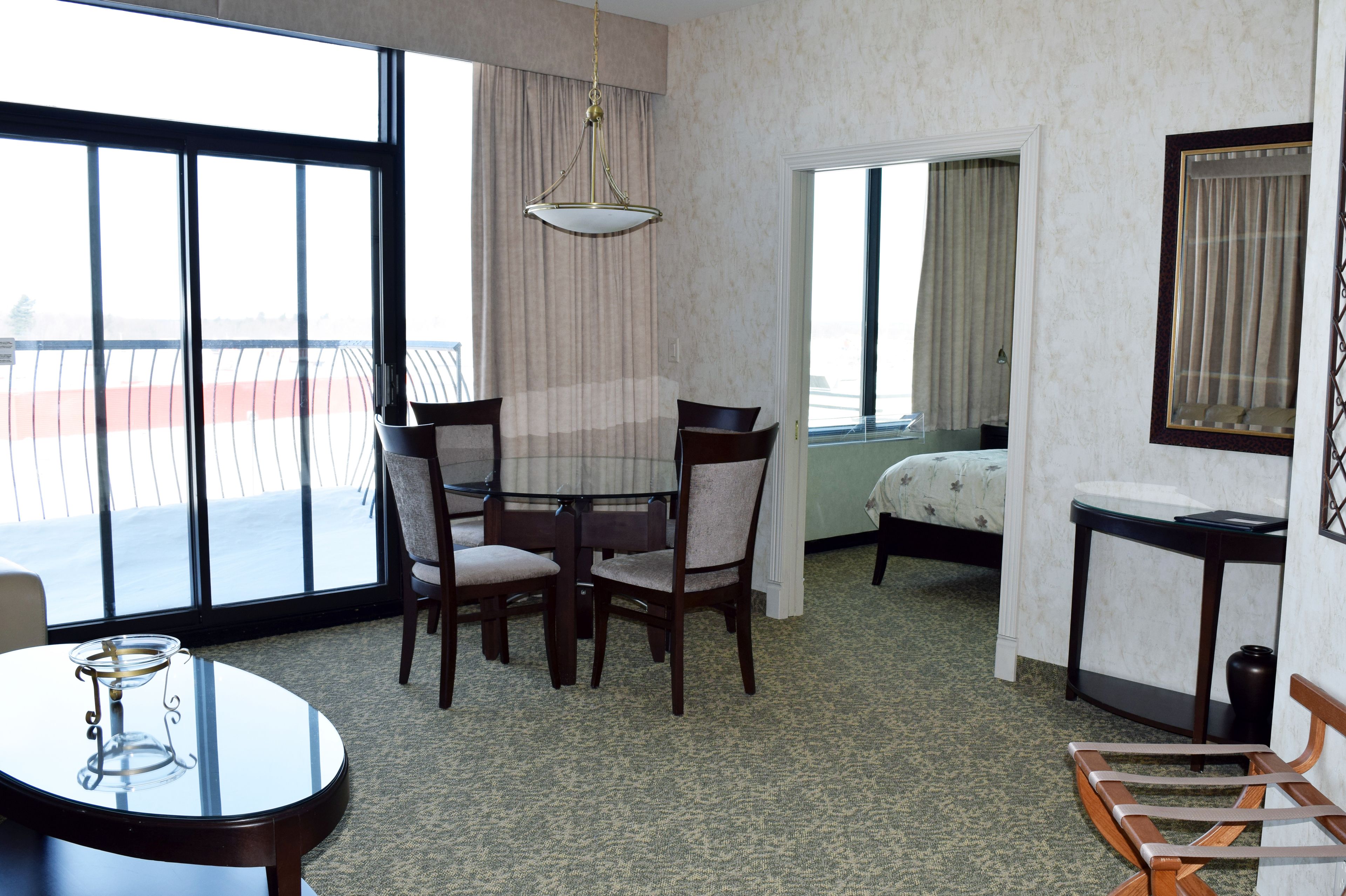 Habitación de hotel con balcón, una mesa de comedor con sillas, una cama y una mesita con un jarrón.