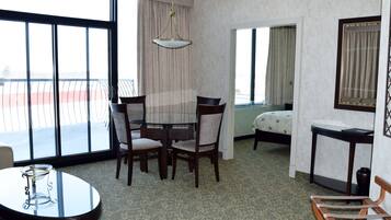 Habitación de hotel con balcón, una mesa de comedor con sillas, una cama y una mesita con un jarrón.