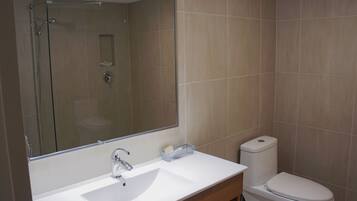 Un baño con lavamanos blanco, espejo, inodoro y ducha.