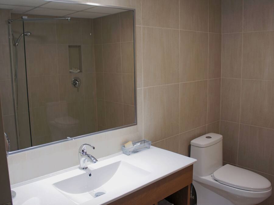 Un baño con lavamanos blanco, espejo, inodoro y ducha.