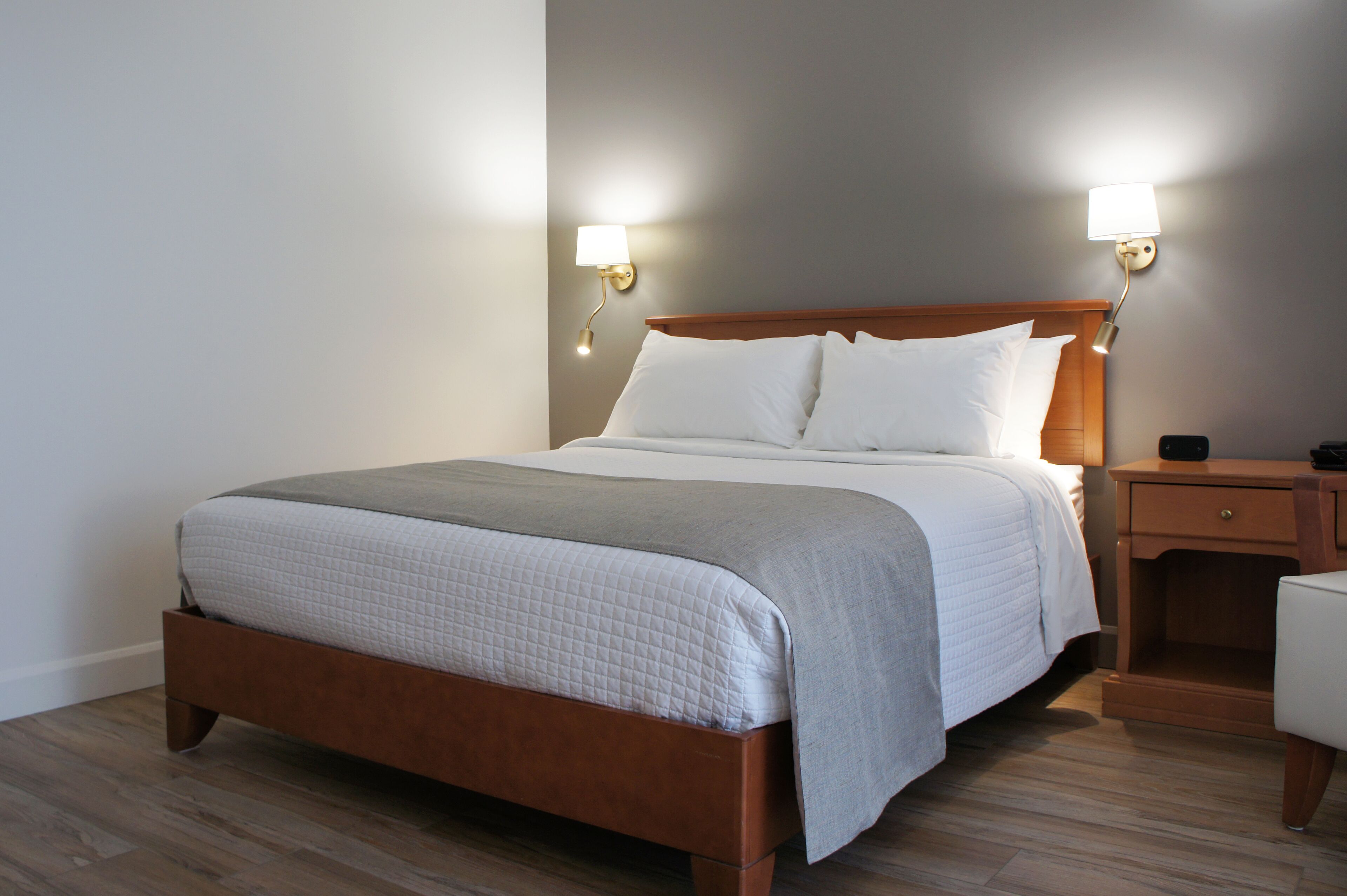 A neatly made bed with a wooden headboard, two bedside lamps, and a wooden nightstand with a drawer.
