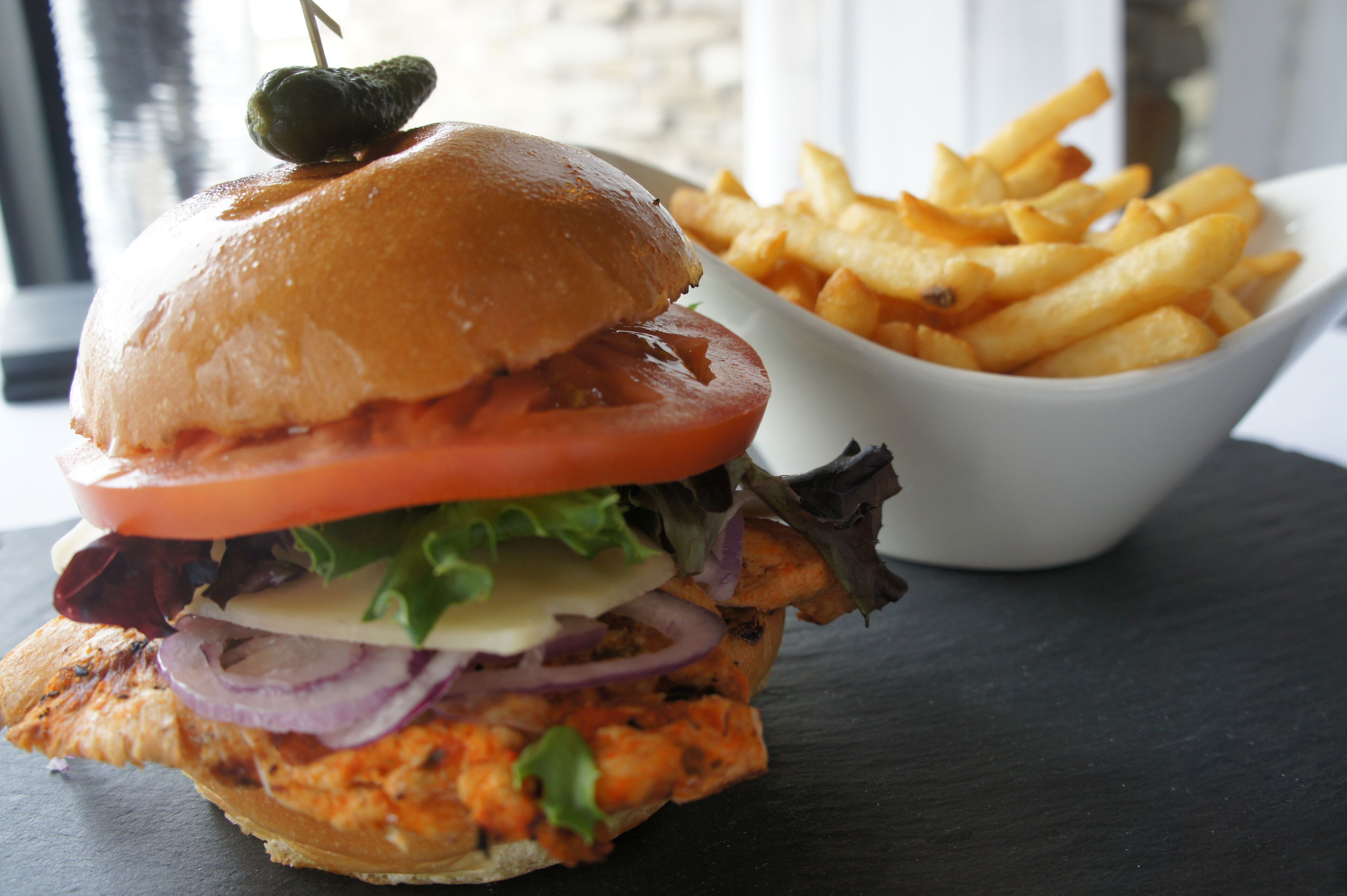 A burger with a tomato slice, lettuce, and a grilled patty, accompanied by a bowl of French fries.