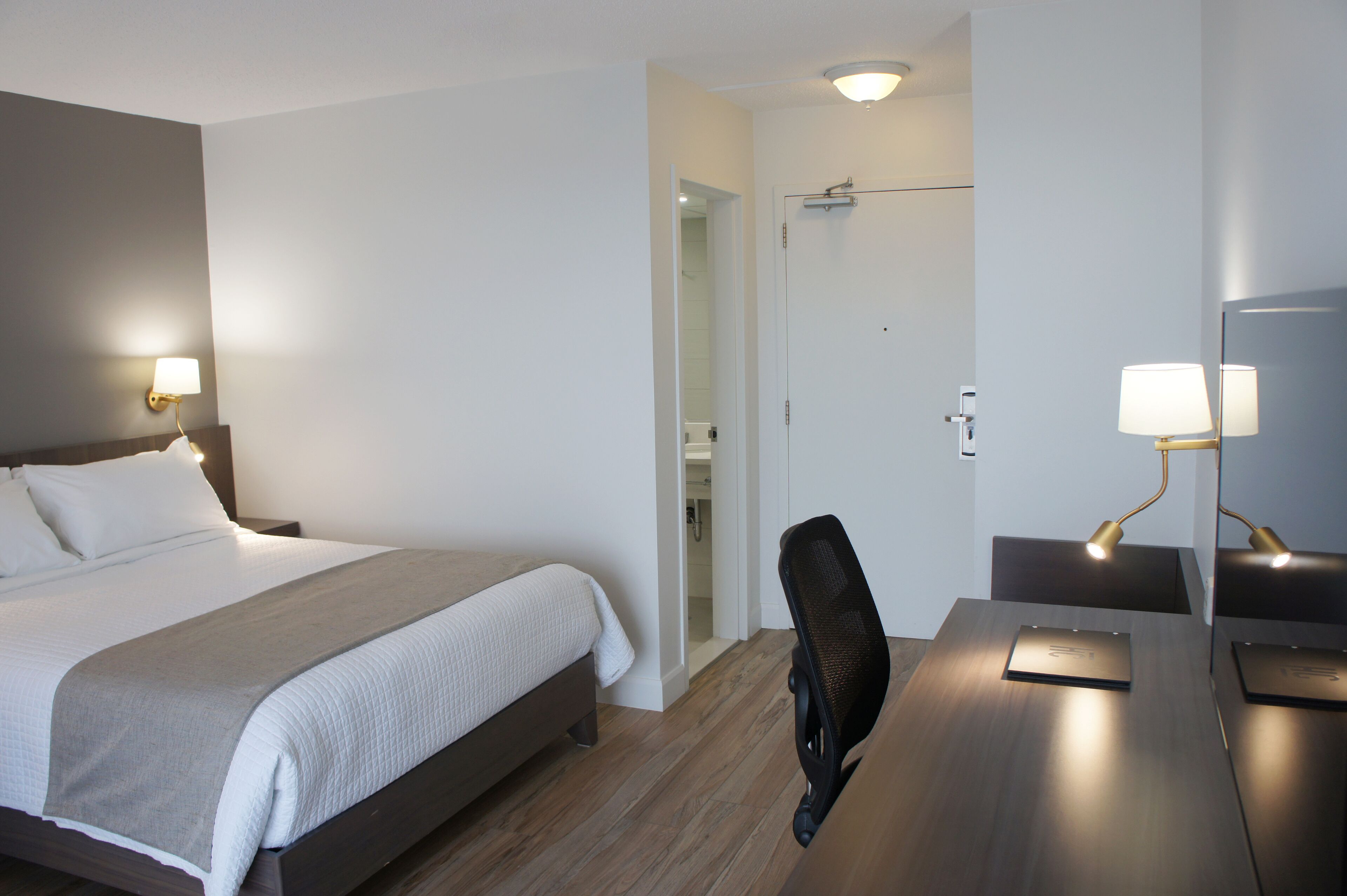 Une chambre d’hôtel comprenant un lit, des lampes de chevet, un bureau avec une chaise et une porte donnant sur une salle de bain.