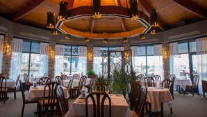 Un restaurante con vigas de madera en el techo, ventanas amplias y mesas dispuestas para comer.