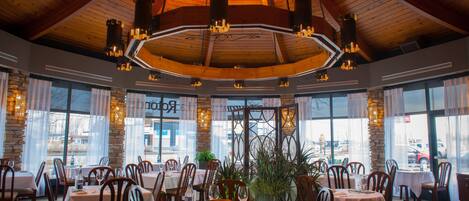 A restaurant with wooden ceiling beams, large windows, and tables set for dining.