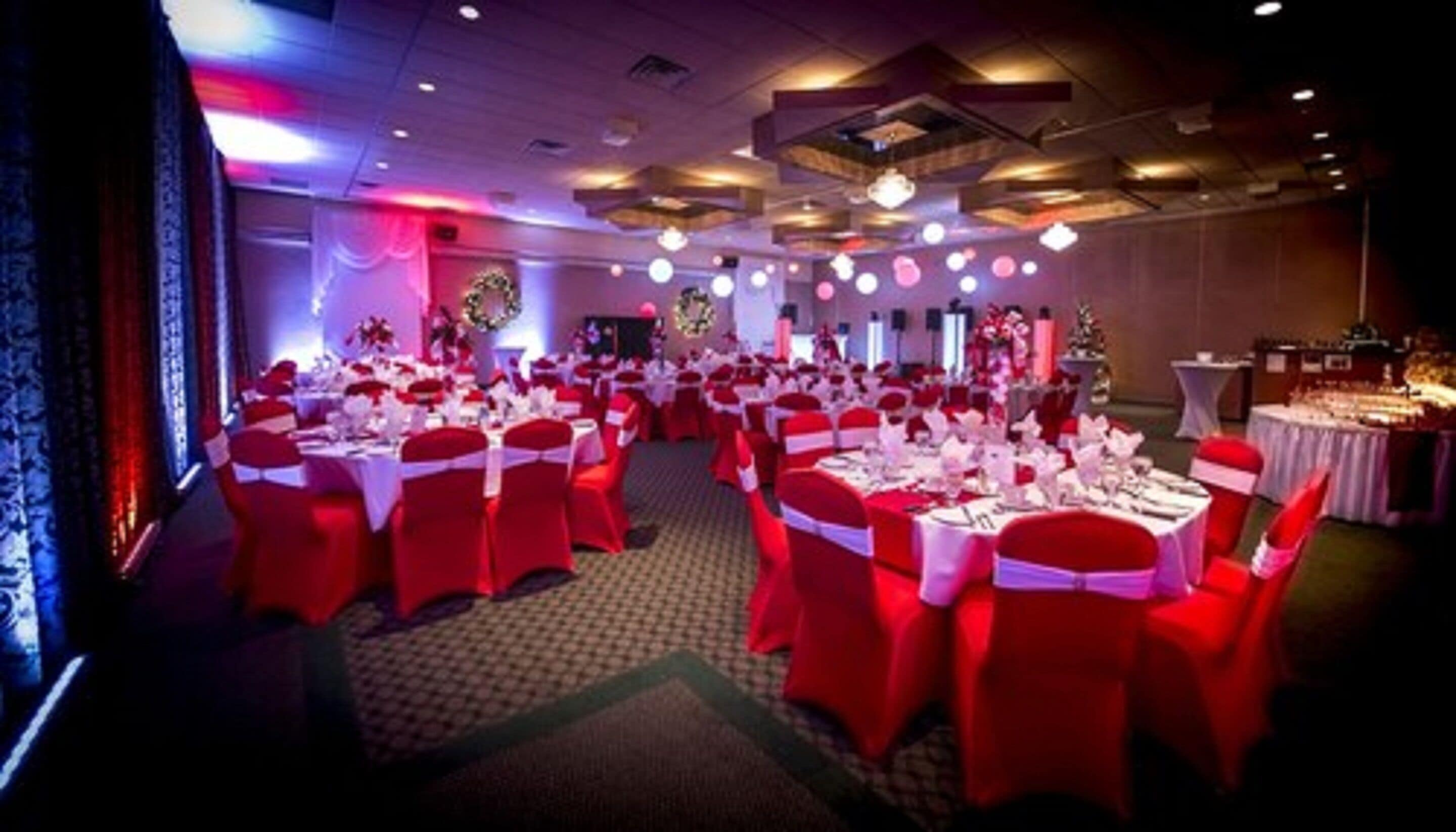 Un salón de banquetes con mesas redondas cubiertas con manteles blancos y sillas rojas.