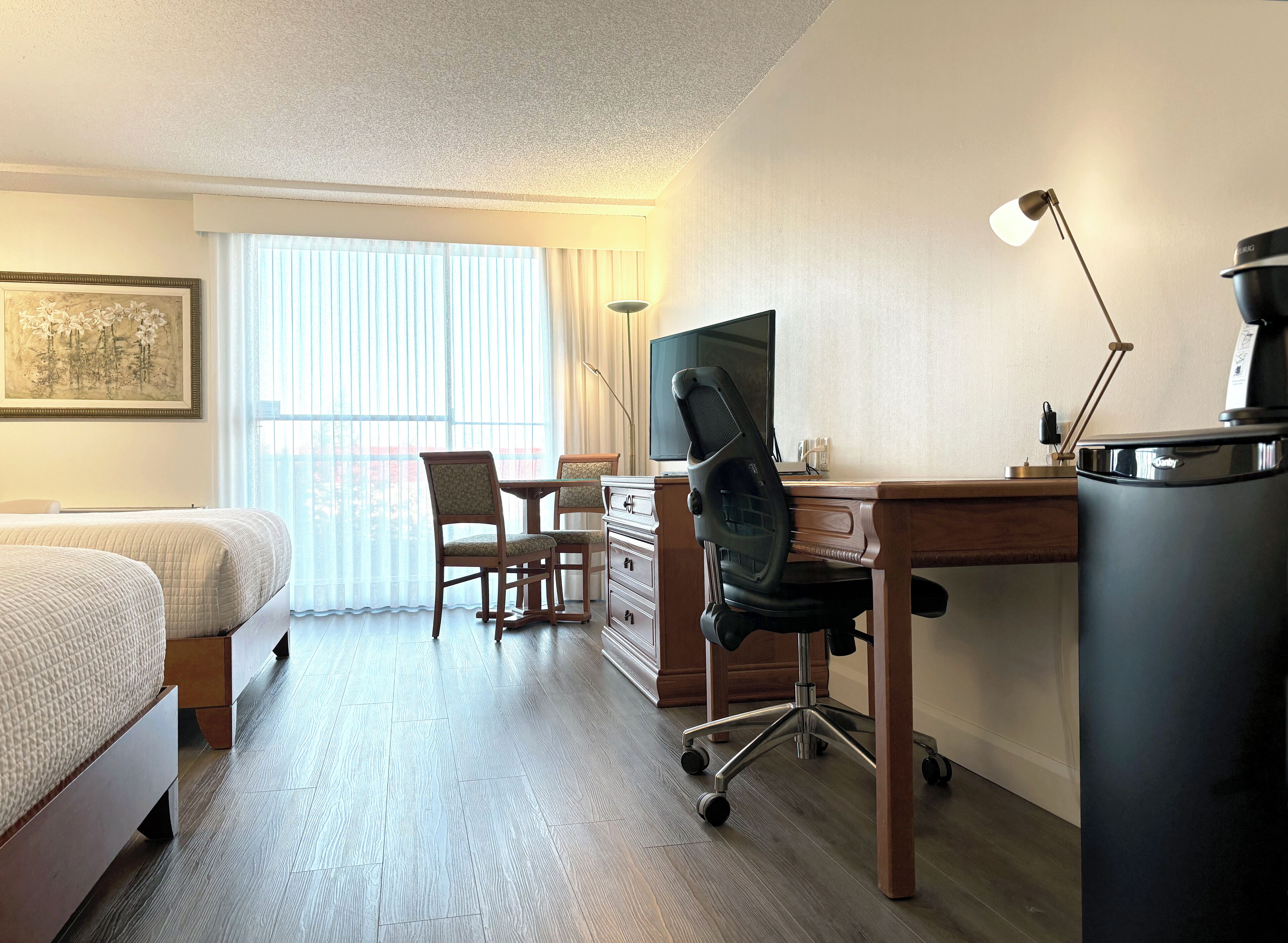 Habitación de hotel con una cama, un escritorio con computadora, una silla, televisor, lámpara y un cubo de basura.