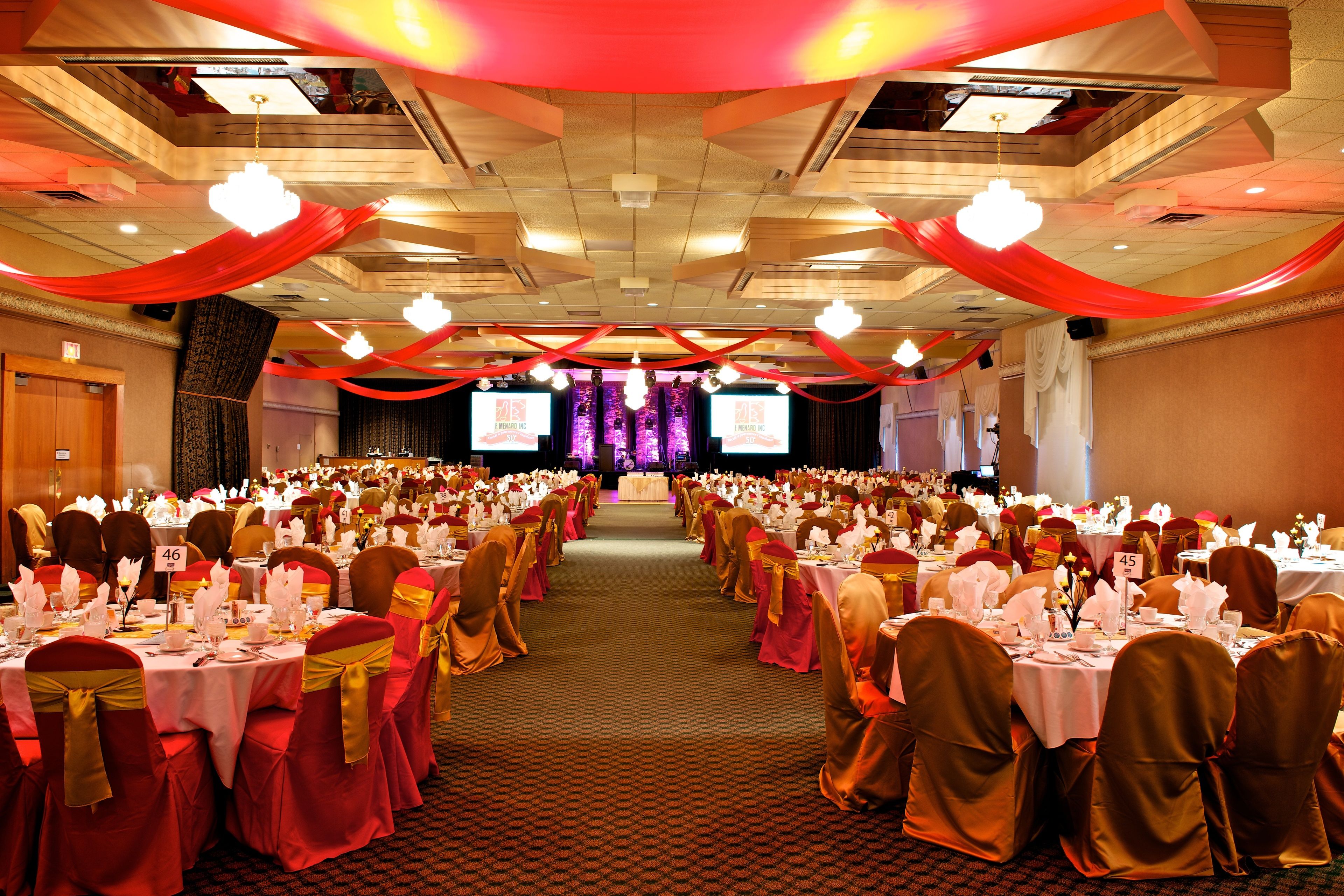 A banquet hall with rows of tables set for a formal event, featuring a central stage and a carpeted floor.