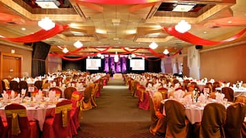 A banquet hall with rows of tables set for a formal event, featuring a central stage and a carpeted floor.