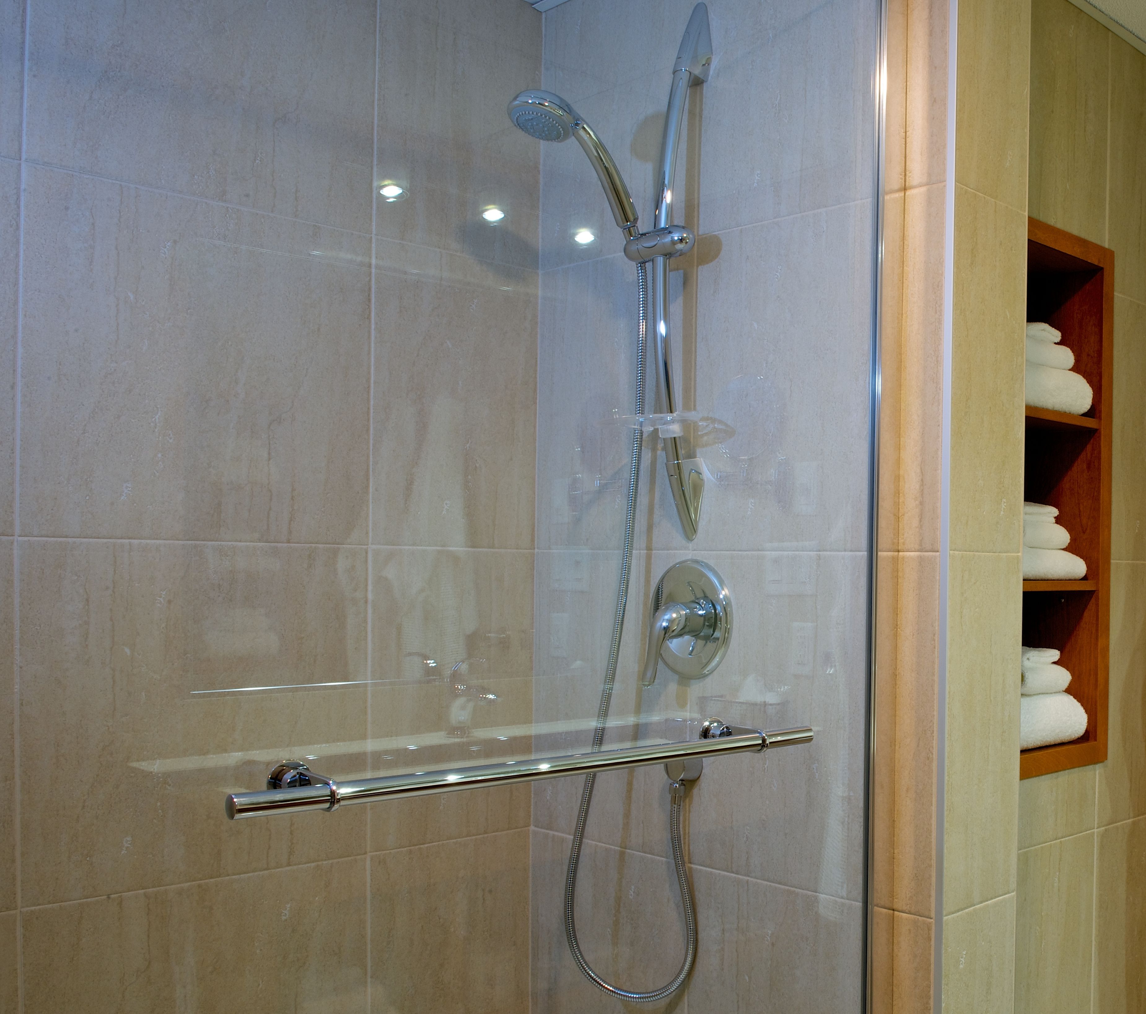 A glass-enclosed shower with a handheld showerhead, a wall-mounted faucet, and a handheld showerhead.