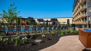 A pool area with lounge chairs and a hot tub, surrounded by a fence and landscaped garden.