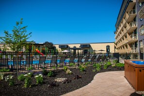A pool area with lounge chairs and a hot tub, surrounded by a fence and landscaped garden.