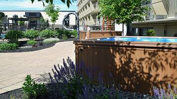 A hot tub in a landscaped outdoor area with a pool, surrounded by plants and a building with balconies.