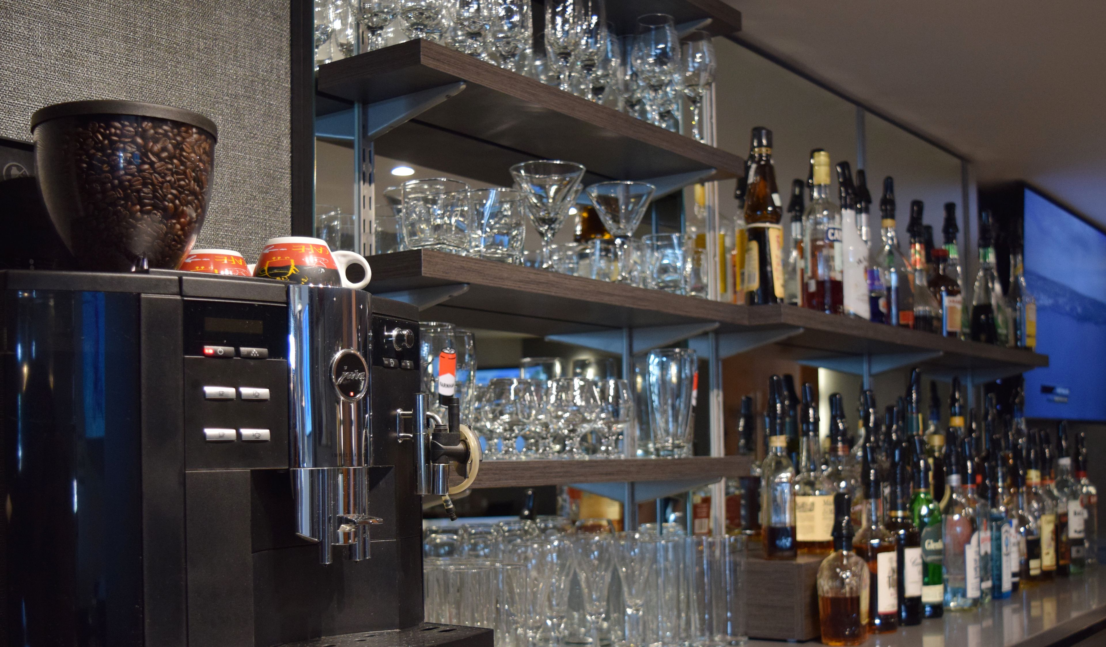 A bar area with shelves of glassware and bottles, a coffee machine, and a coffee cup with a bean pattern.