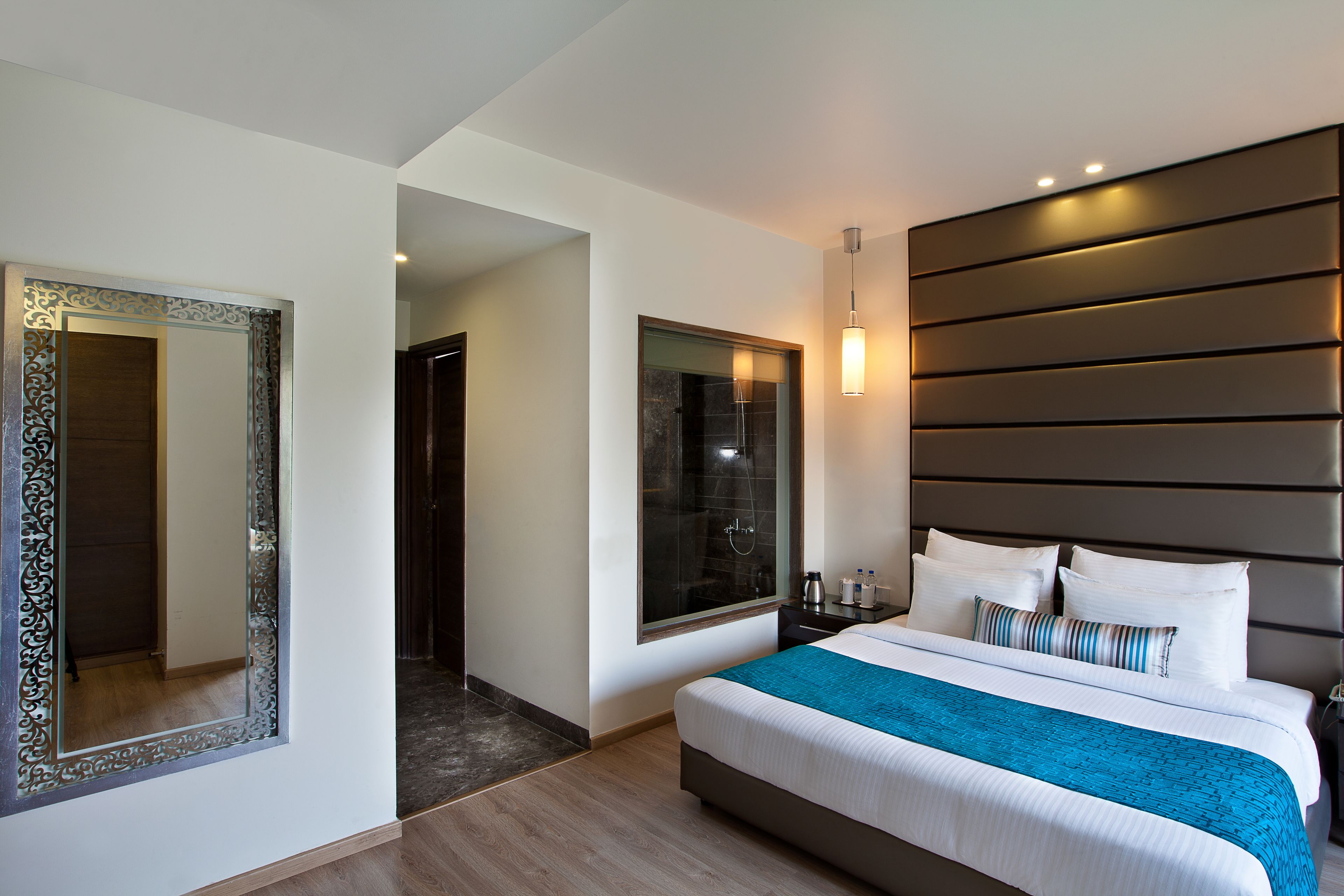 A modern hotel room with a large bed, a mirror, a shower area, and a bedside table with a lamp.