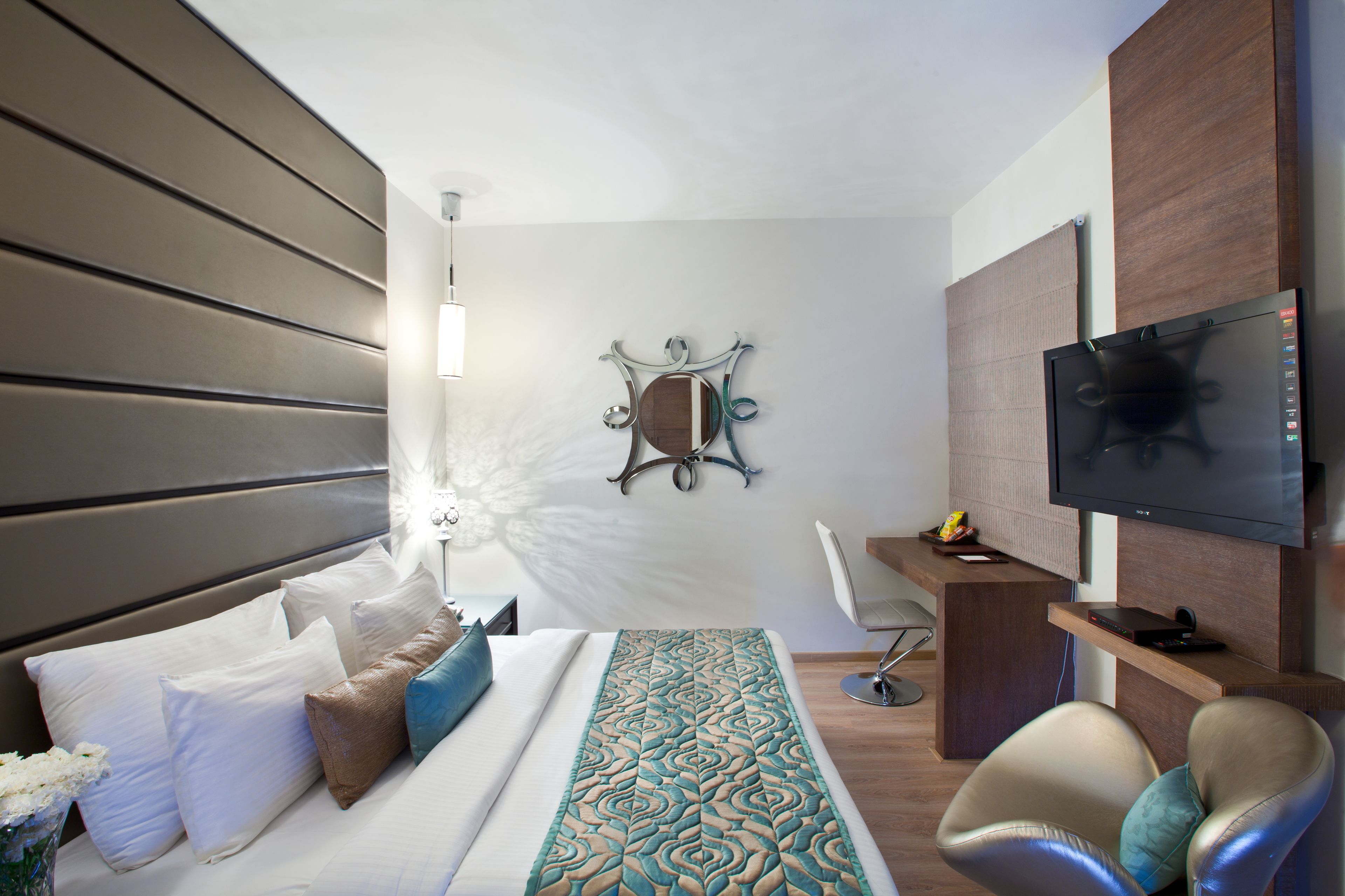 A modern hotel room with a bed, a desk, a television, and a decorative mirror.