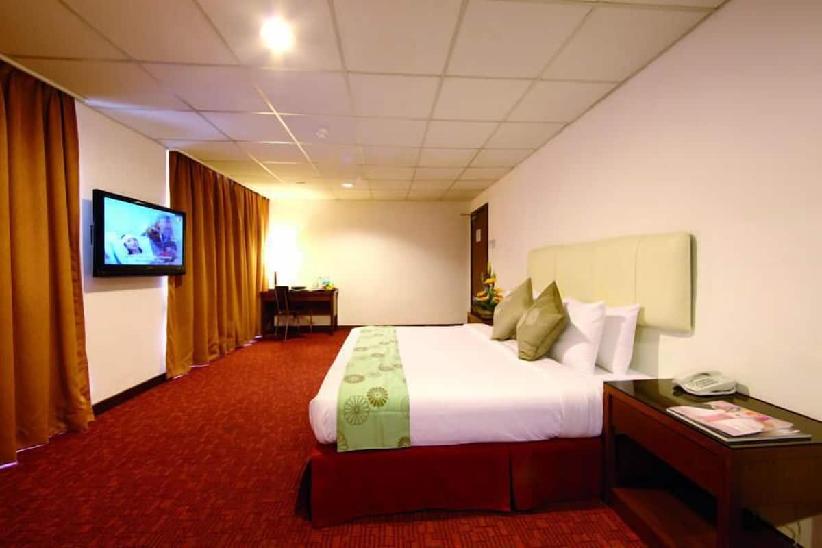 A hotel room with a bed, a television on the wall, a desk, and a telephone.