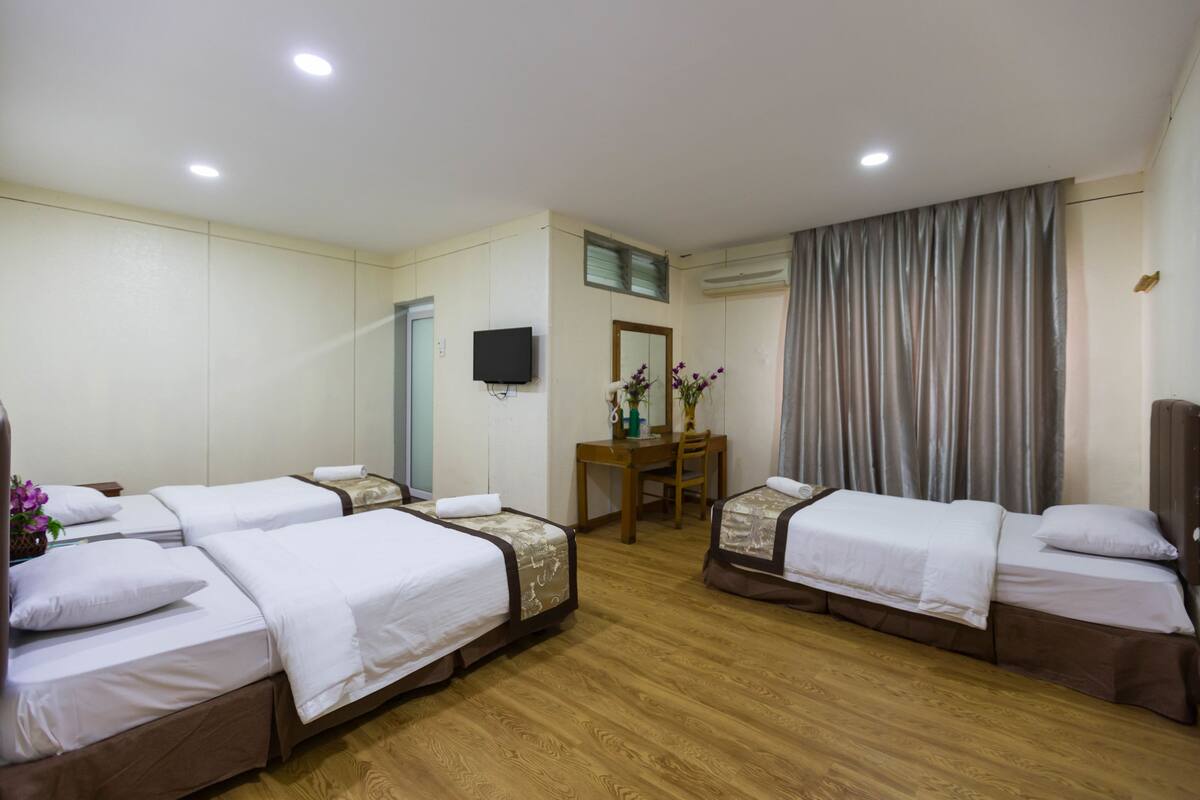 A hotel room with four single beds, a desk, a chair, a flat-screen TV, and a window with curtains.