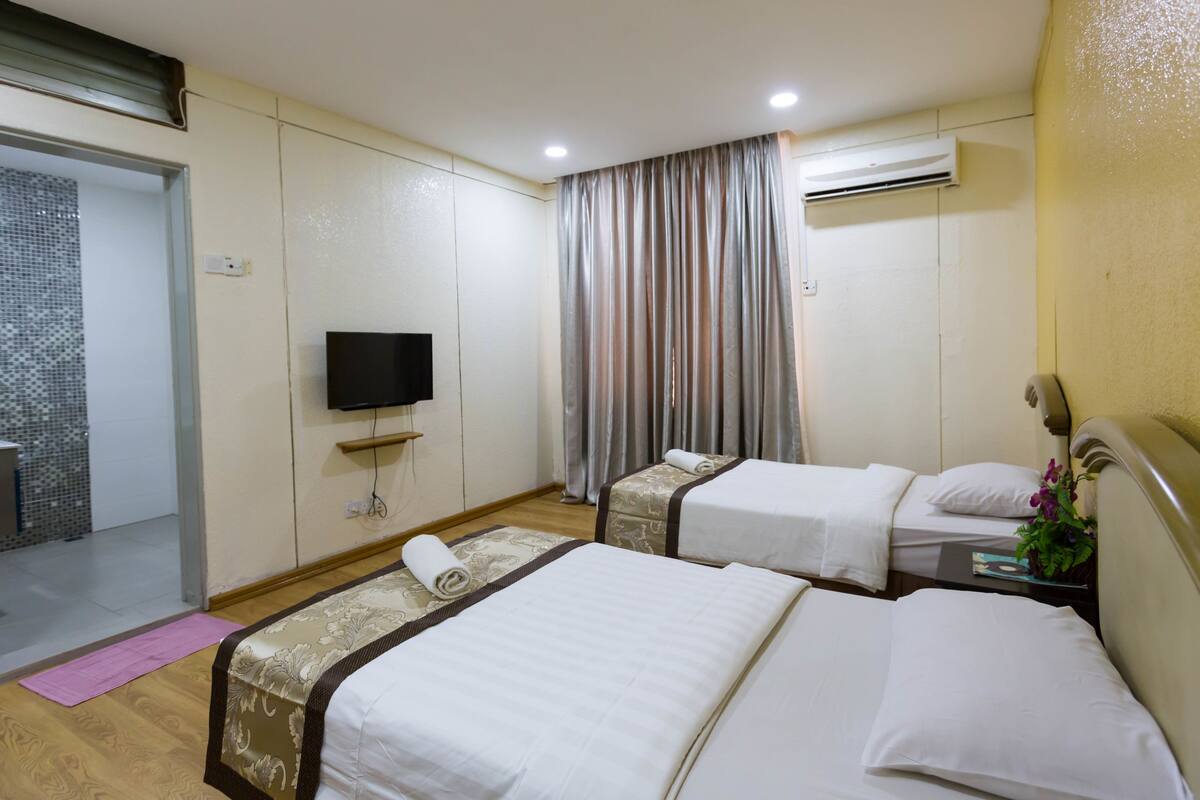 A hotel room with two beds, a television, an air conditioning unit, and a bathroom with a shower.