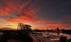 A sunset over a body of water with a small white building and a tree in the foreground. - The Ranee Boutique Suites (Kuching)