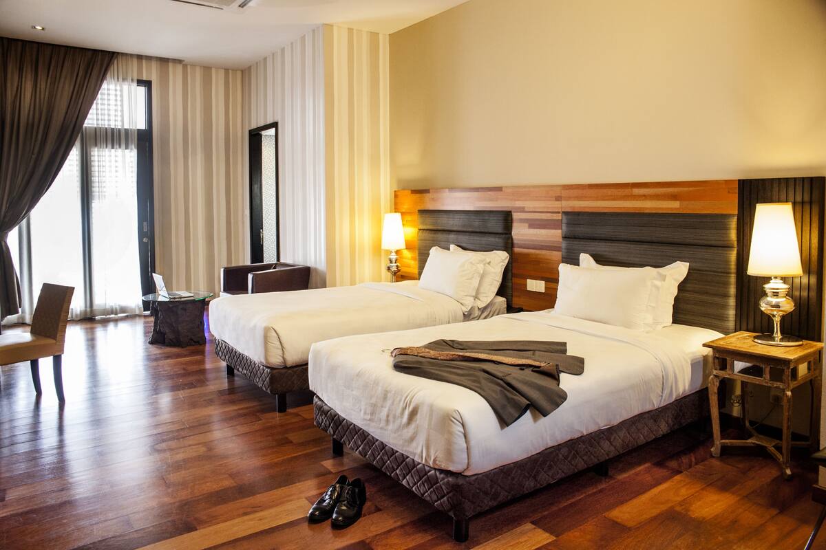 A hotel room with two beds, a desk, a chair, and a lamp.