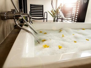 A bathtub with bubbles and yellow flowers, a black chair, and a reflection of a person in the background. - The Ranee Boutique Suites (Kuching)