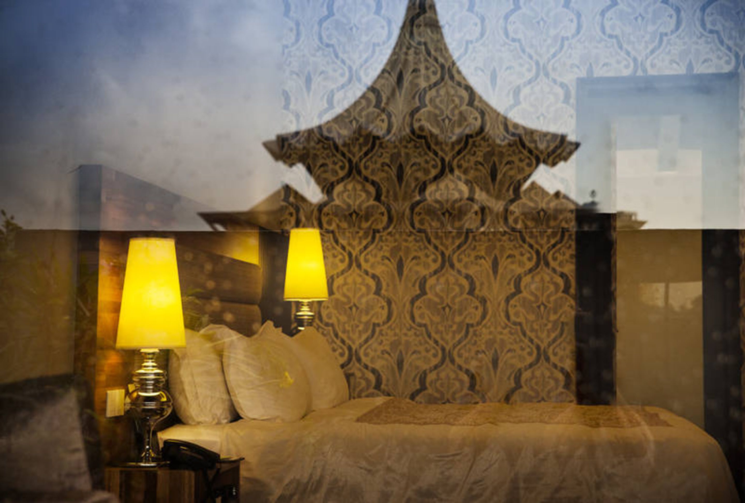 A bed with a patterned headboard, two bedside lamps, and a telephone on a bedside table.