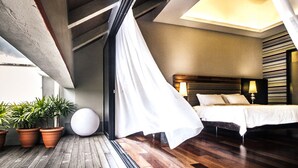 Un dormitorio con piso de madera, una cama con ropa de cama blanca, un objeto redondo y grande de color blanco y plantas en macetas.