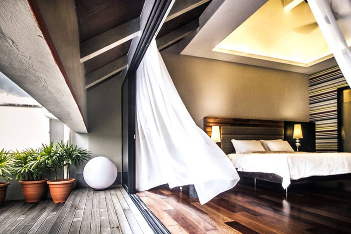 A bedroom with a wooden floor, a bed with white bedding, a large round white object, and potted plants.