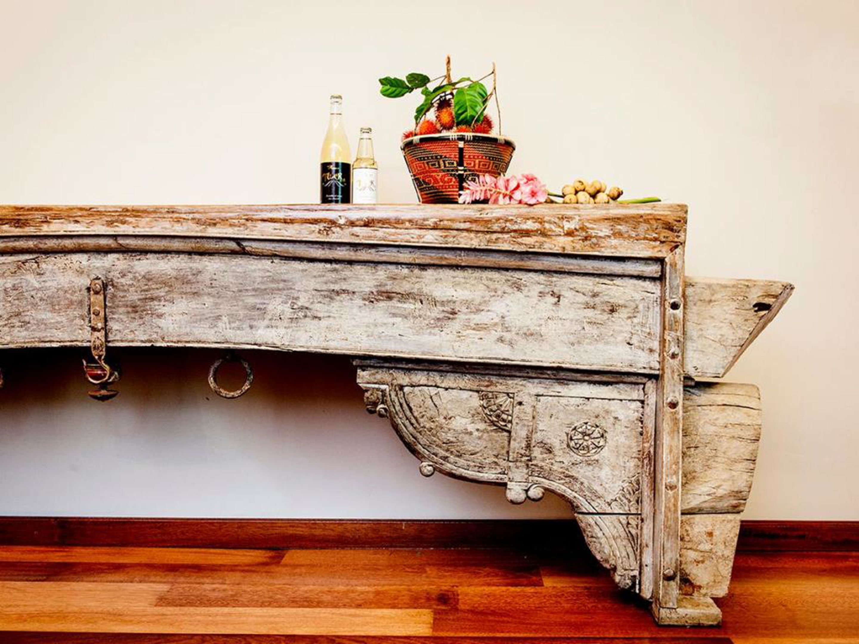 A rustic wooden table with a decorative basket, two bottles, and a potted plant.