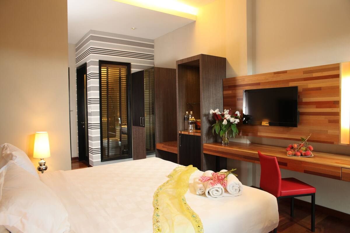 A hotel room with a large bed, a desk with a TV, a red chair, and a wooden wall panel.