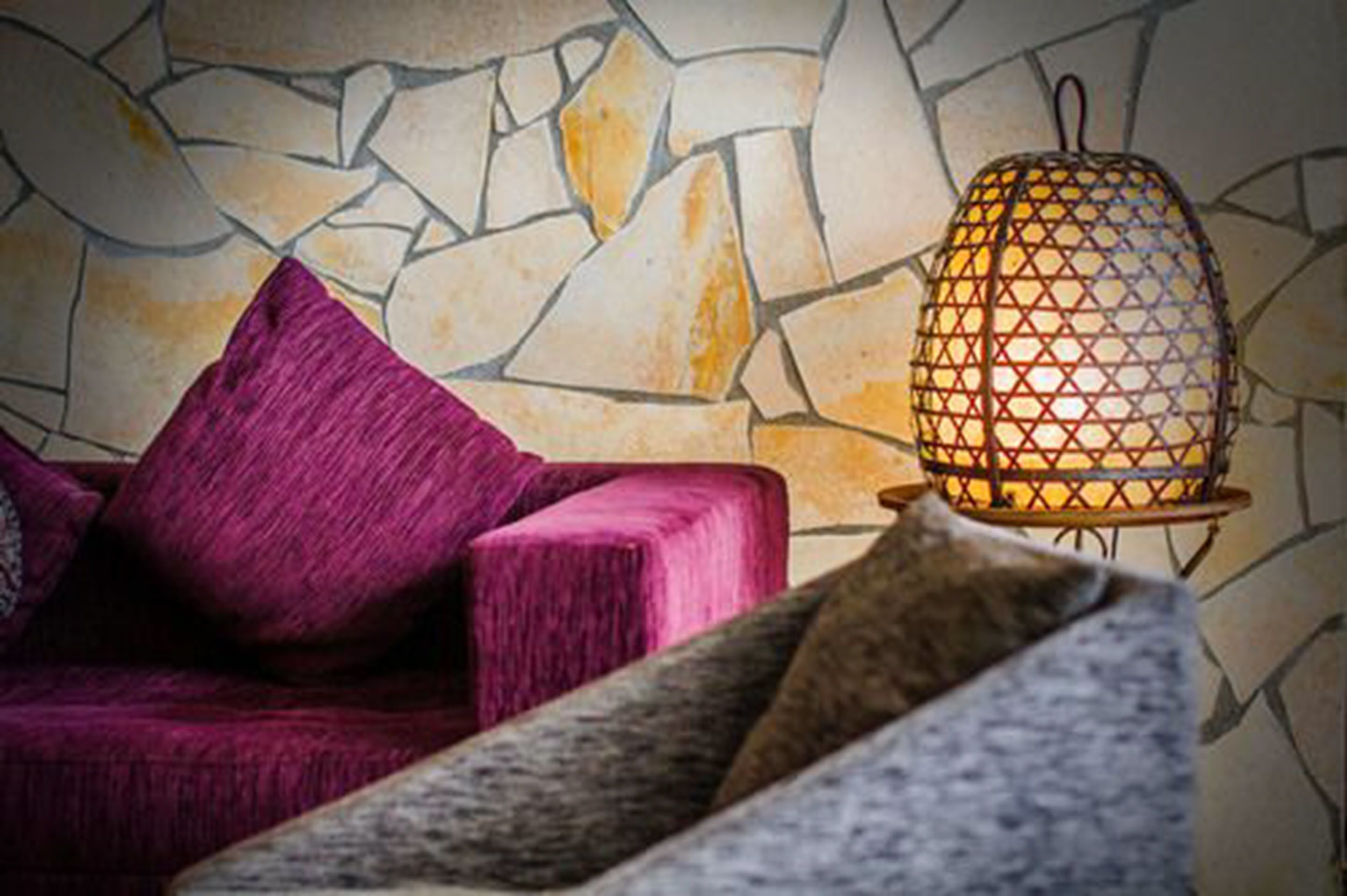 Um quarto com parede de pedra, sofá roxo e luminária estampada.