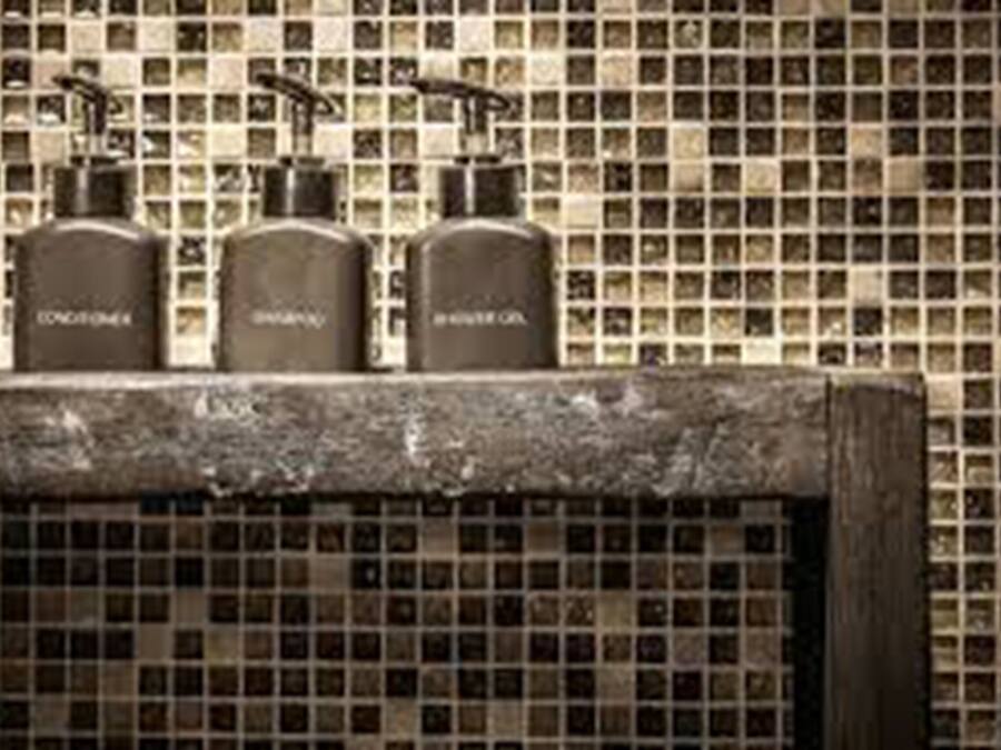 A bathroom with a tiled backsplash and three bottles labeled "CONDOMINIUM," "SHAMPOO," and "SHOWER GEL" on a shelf.