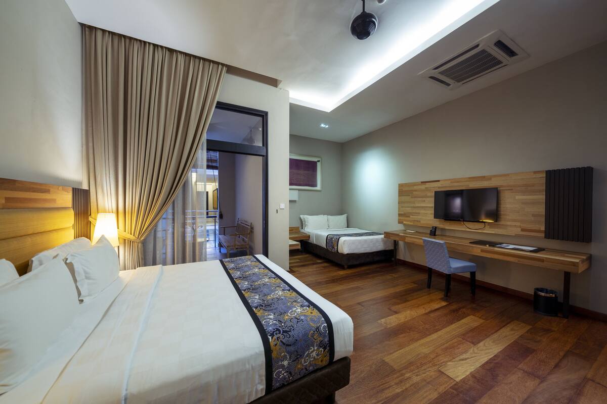 A hotel room with a large bed, a desk, a chair, a TV, and a wooden floor.