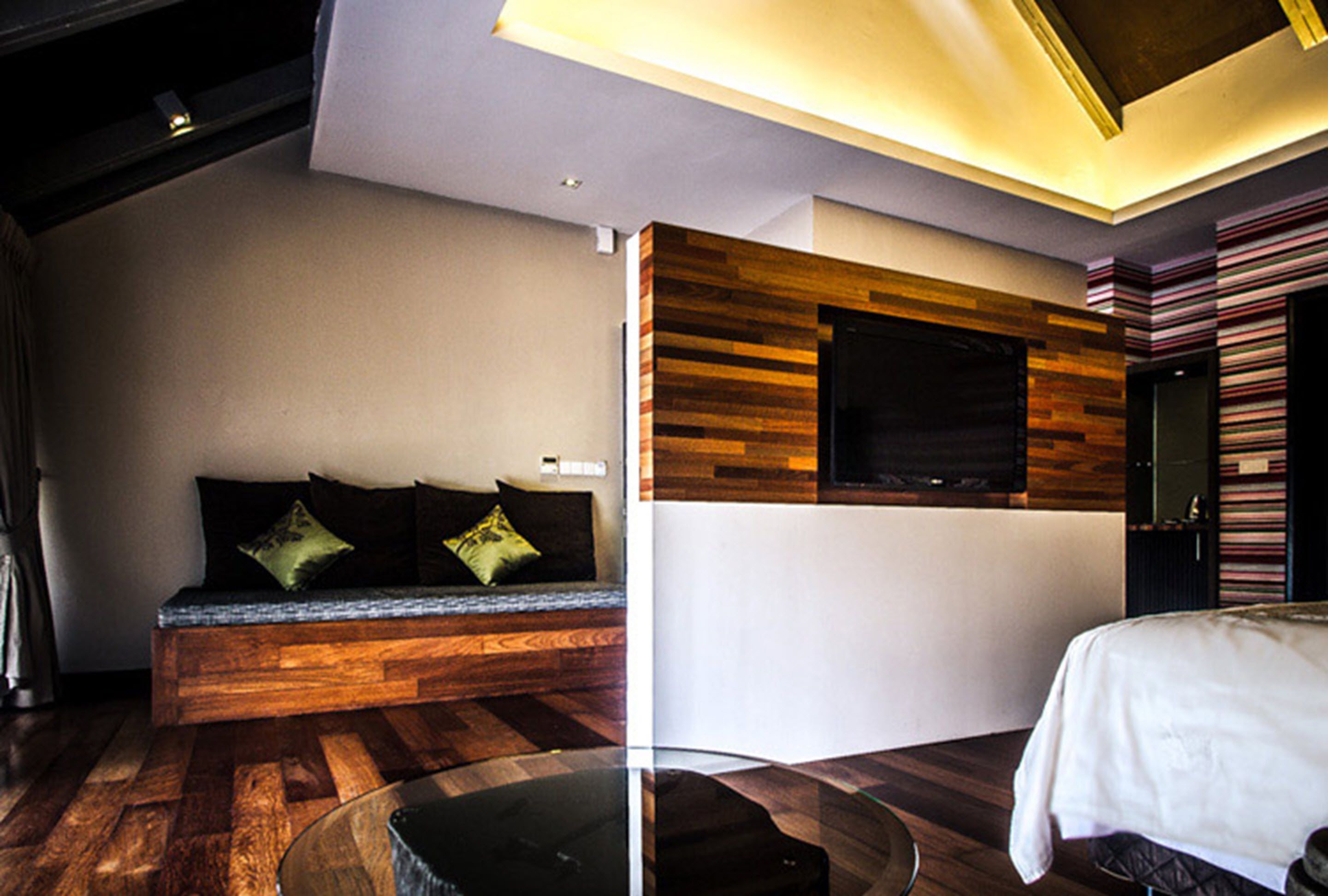 Een moderne hotelkamer met een wand van hout, een glazen salontafel, een bank met kussens en een bed met witte hoes.
