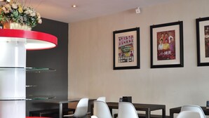 A modern restaurant interior with a central red and white counter, white chairs, and framed pictures on the wall.