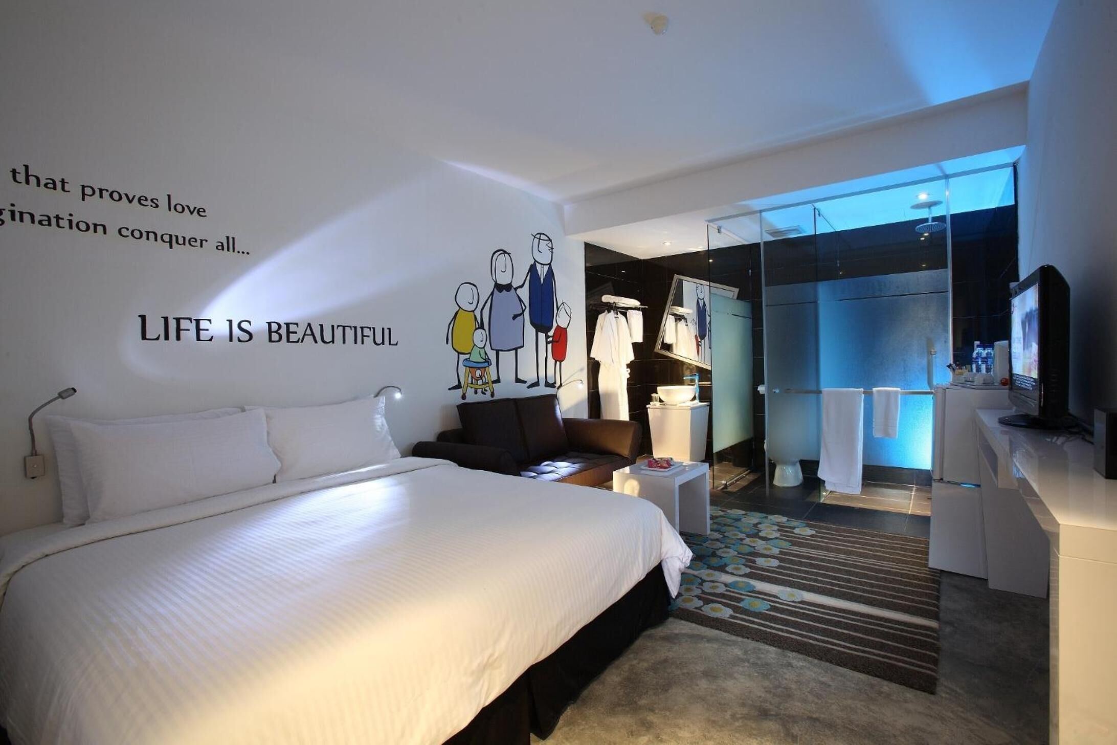 Une chambre d’hôtel moderne dotée d’un grand lit, d’un petit coin salon, d’une douche en verre et d’une coiffeuse avec un miroir.